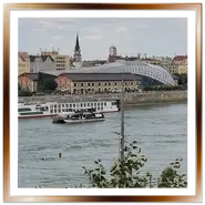 L'avveniristico edificio Bálna, denominato "La Balena", sulla sponda del fiume Danubio a Budapest, visto dal lato di Buda con battelli in transito e passanti in primo piano.