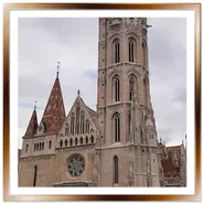 Facciata della Chiesa di Mattia a Budapest durante un tour guidato nel quartiere di Buda, con l'imponente torre campanaria gotica, il rosone centrale e turisti sulla piazza sotto un cielo coperto e nuvoloso.