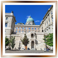 Vista del cortile interno del Palazzo Reale nel Castello di Buda a Budapest, con l'imponente scalinata in pietra bianca, la cupola verde dell'edificio principale sullo sfondo e alberi decorativi sotto un cielo blu limpido.