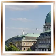 Primo piano della cupola verde del Palazzo Reale di Buda con la bandiera ungherese e, sullo sfondo, la Statua della Libertà sulla cima della collina Gellért sotto un cielo sereno.