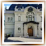 Facciata dell'edificio storico del Maneggio Reale (Lovarda) nel Castello di Buda a Budapest, con il tetto decorato scuro e, in primo piano sulla sinistra, la statua in bronzo del domatore con cavallo rampante.