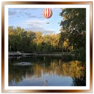 Mongolfiera rossa e bianca Balloon Fly in volo sul laghetto del Parco Cittadino di Budapest con riflesso nell'acqua
