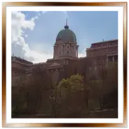 Facciata imponente e grande cupola verde del Palazzo Reale (Castello di Buda) a Budapest, visto dal basso della collina con alberi e grandi nuvole nel cielo.