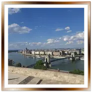 Spettacolare panorama di Budapest visto dalla collina di Buda, con il Ponte delle Catene sul Danubio, il Parlamento ungherese sullo sfondo e la città di Pest sotto un cielo azzurro e nuvoloso.