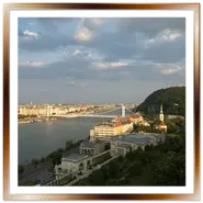 Vista panoramica sul fiume Danubio a Budapest dal castello di Buda, con il Ponte Elisabetta, la collina Gellért e il lungofiume sullo sfondo sotto un cielo nuvoloso.