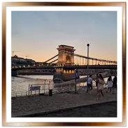 Il secolare Ponte delle Catene illuminato al tramonto a Budapest, visto dal lungofiume di Pest con persone che passeggiano.