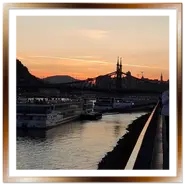 Grandi navi da crociera ormeggiate sul Danubio a Pest al tramonto, con il profilo del Ponte della Libertà sullo sfondo e passanti sul lungofiume.