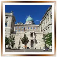 Prospettiva dal basso della doppia scalinata in pietra chiara e della cupola verde del Palazzo Reale nel complesso del Castello di Buda a Budapest, sotto un cielo limpido.