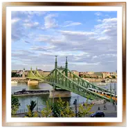 Vista dall'alto del Ponte della Libertà (Szabadság híd) in ferro verde a Budapest, con un tipico tram giallo che lo attraversa, battelli in navigazione sul fiume Danubio e la sponda di Pest sotto un cielo parzialmente nuvoloso.