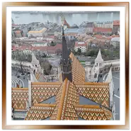 Veduta dall'alto del tetto con tegole colorate geometriche della Chiesa di Mattia e del Bastione dei Pescatori a Buda, con panorama sul Danubio e sul Parlamento di Budapest sullo sfondo.