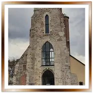 Antica torre campanaria gotica della Chiesa di Maria Maddalena a Buda, Budapest, con i resti archeologici medievali in primo piano sotto un cielo nuvoloso.