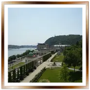 Veduta panoramica dall'alto del Várkert Bazár a Budapest, con i giardini curati, la fontana circolare, i loggiati ricoperti di rampicanti, il Danubio a sinistra con il Ponte Elisabetta e il monte Gellért sullo sfondo.