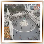 Vista panoramica dall'alto del Bastione dei Pescatori e della statua di Santo Stefano dal campanile della Chiesa di Mattia a Budapest, con il tetto in maiolica colorata in primo piano e il Danubio sullo sfondo.